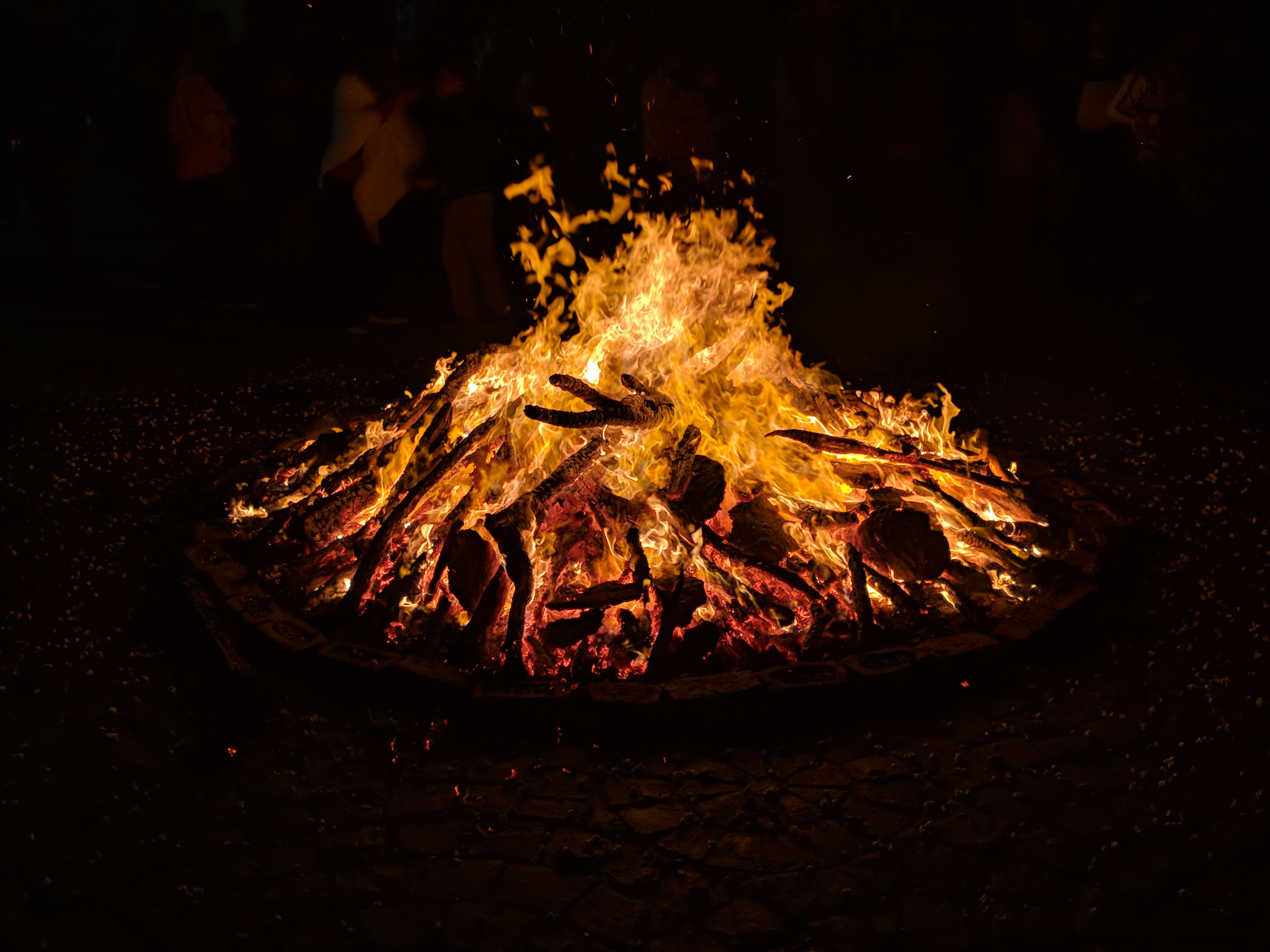 A bonfire at night time. The background is entirely black, and the bonfire is burning orange and yellow.