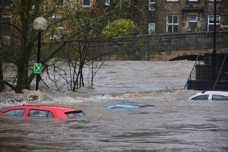 A red car, a blue car, and a white car, all submerged in flood water.