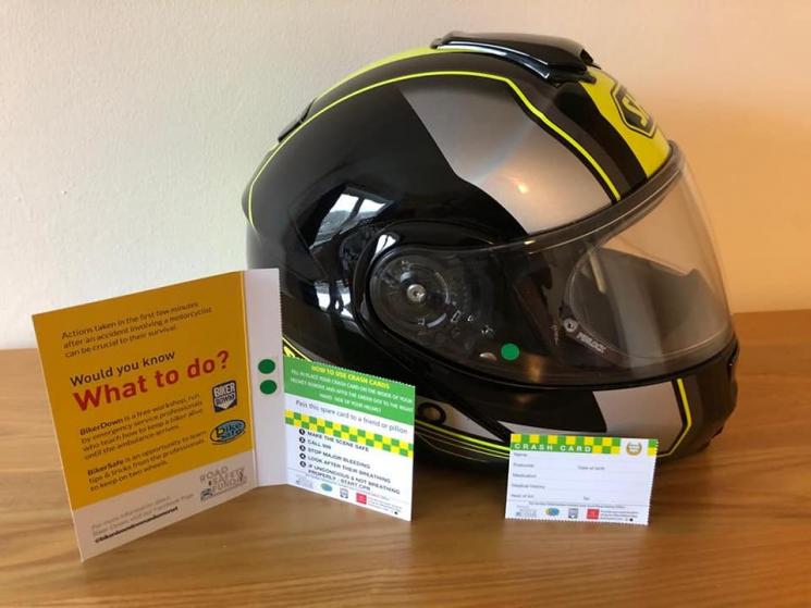 A neon yellow and black helmet with a green sticker on it next to a CRASH Card. The CRASH card is torn off from the information leaflet. It's got a green and red banner across the top, and then has white spaces for filling out the rider's details.  