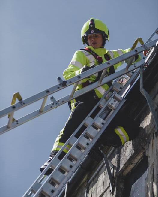 A female firefighter stands on top of a ladder looking down towards the ground.