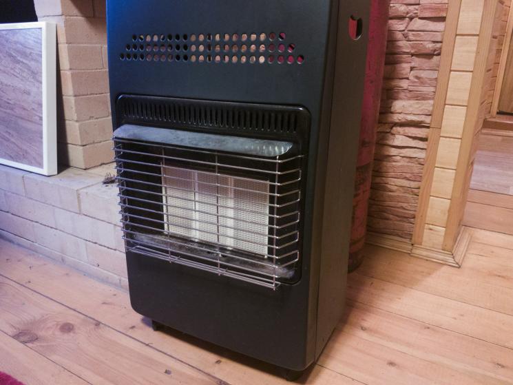 A gas heater, which is black other than the middle where the heat is released, which is white. There are two small black wheels at the front.